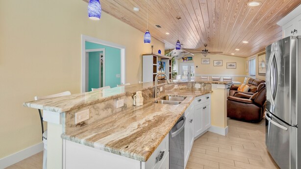 A spacious kitchen with a marble countertop, wooden ceiling, and a built-in refrigerator.