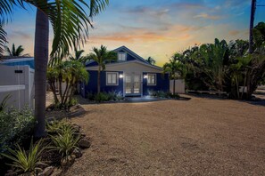 A single-story house with a dark blue exterior, a front porch, and a gravel driveway.