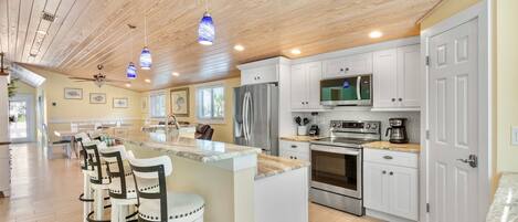A spacious kitchen with a central island, white cabinetry, stainless steel appliances, and a wooden ceiling.
