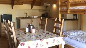 Acogedor interior de cabaña con una mesa de comedor, sillas, una litera y una kitchenette.