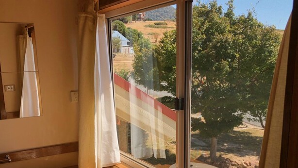 Un baño con tocador de madera, un lavamanos y un amplio ventanal con vistas a una colina y árboles.
