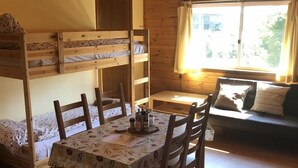 Una cabaña acogedora con literas, una mesa de comedor con sillas y un sofá.