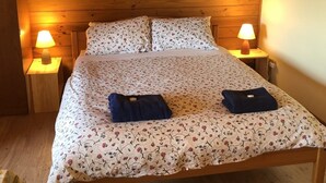 Una habitación acogedora de madera con una cama, dos lámparas de noche y una colcha estampada con motivos florales.
