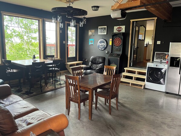 A dining area with a wooden table and chairs, a black leather couch, and a kitchen with a washing machine.