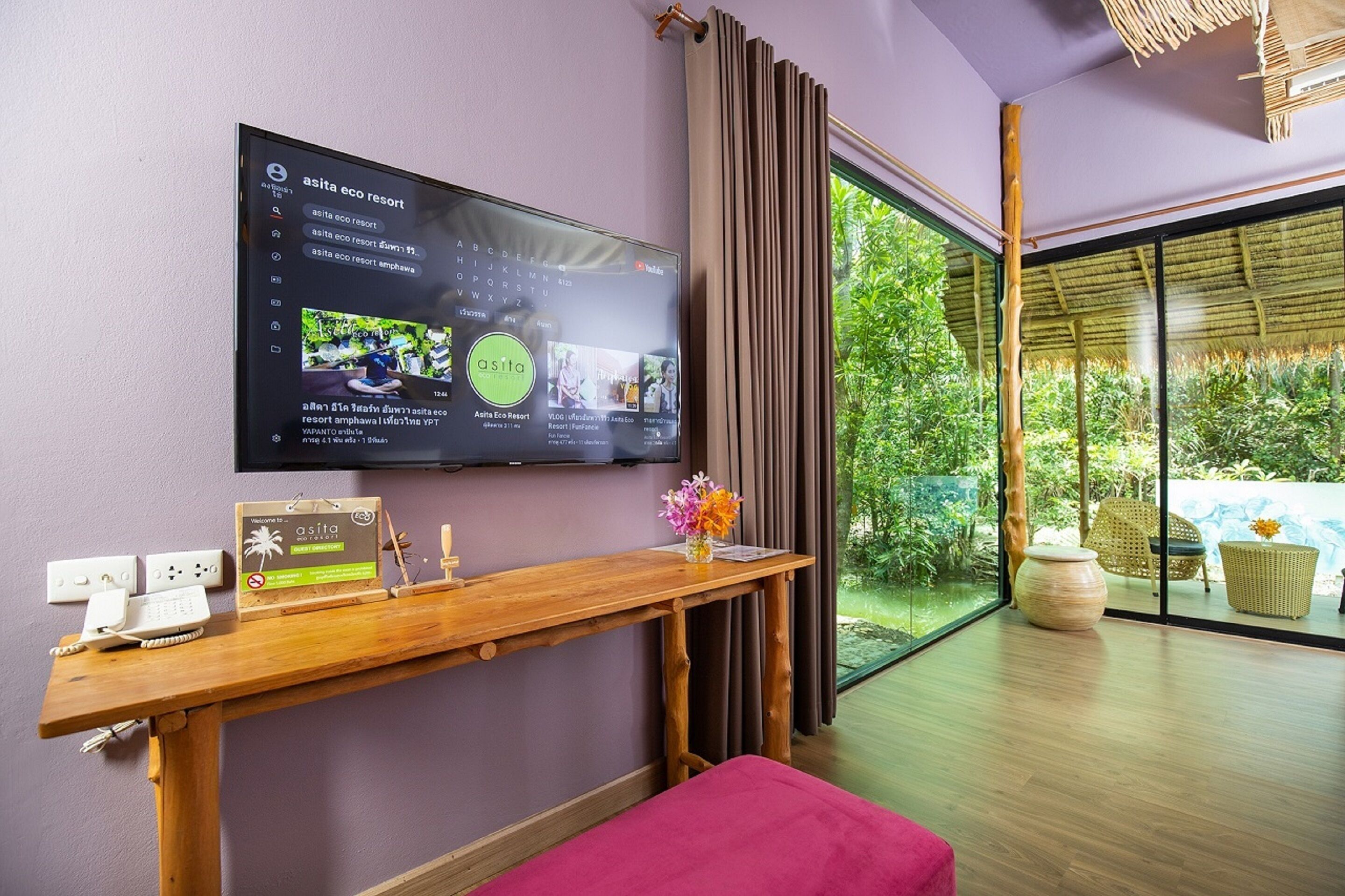 A modern room with a large TV on the wall, a wooden console table, a red bench, and a view of greenery outside.