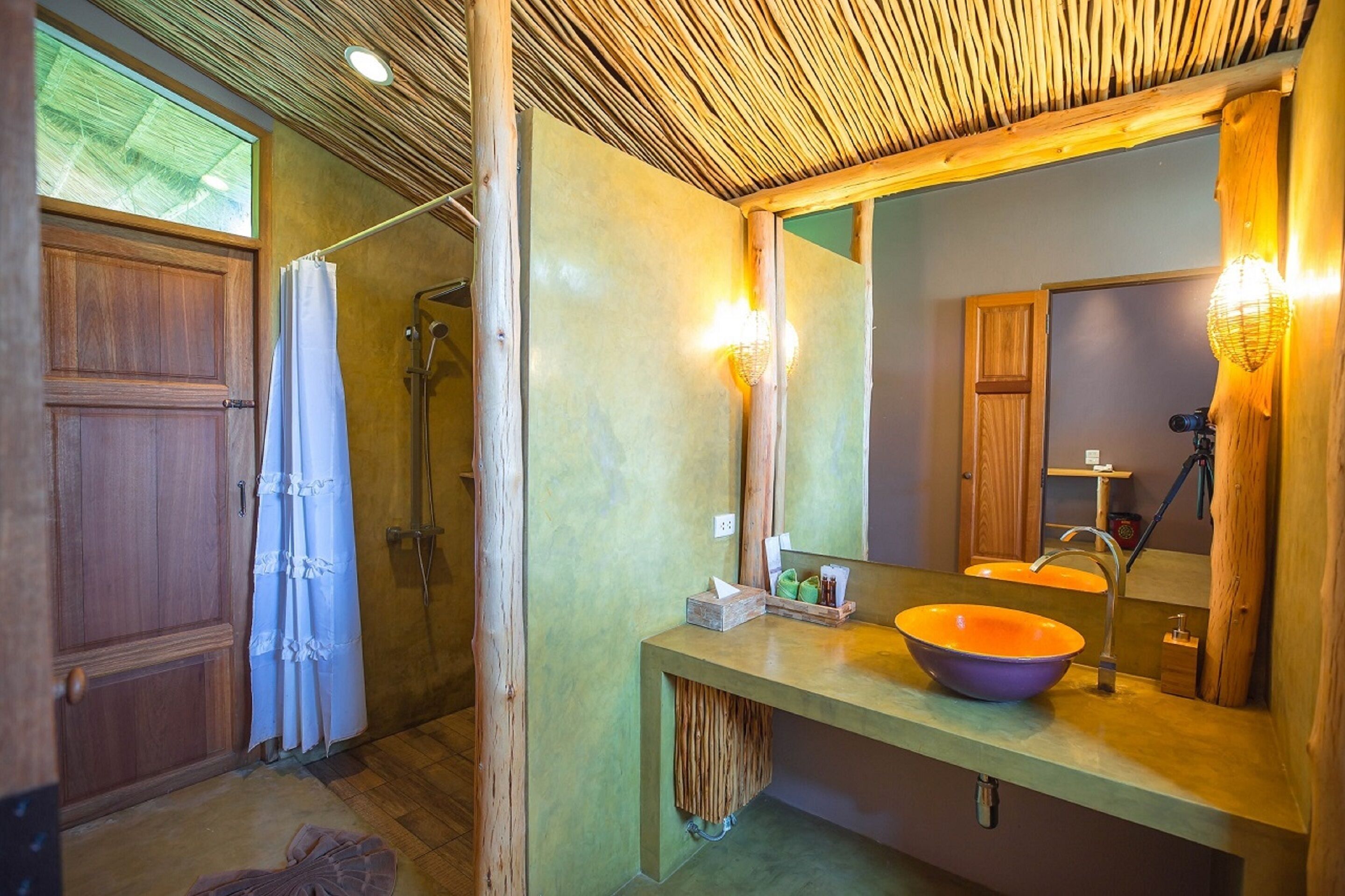A bathroom with a wooden ceiling, a large mirror, and a wooden door.