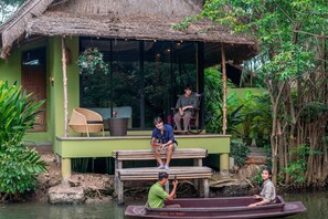 A rustic building with a thatched roof, a bench, and a boat docked outside. - Asita Eco Resort (Samut Songkhram)