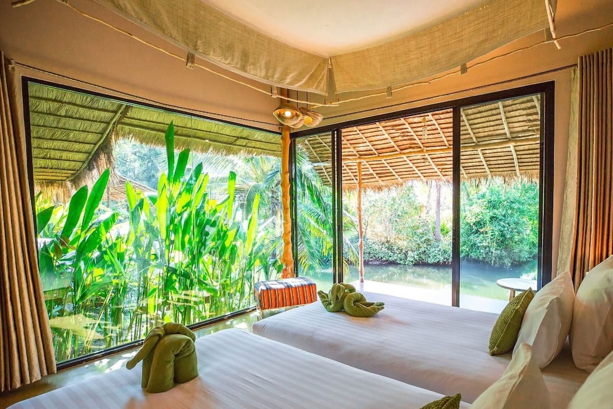 A room with two beds, large windows, and a view of greenery.
