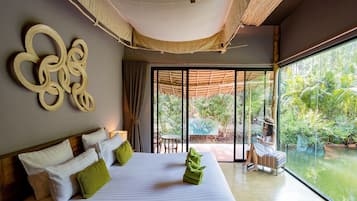 Una habitación de hotel moderna con una cama grande, vista a un jardín exuberante a través de una puerta corrediza de vidrio y una pieza decorativa original en la pared.