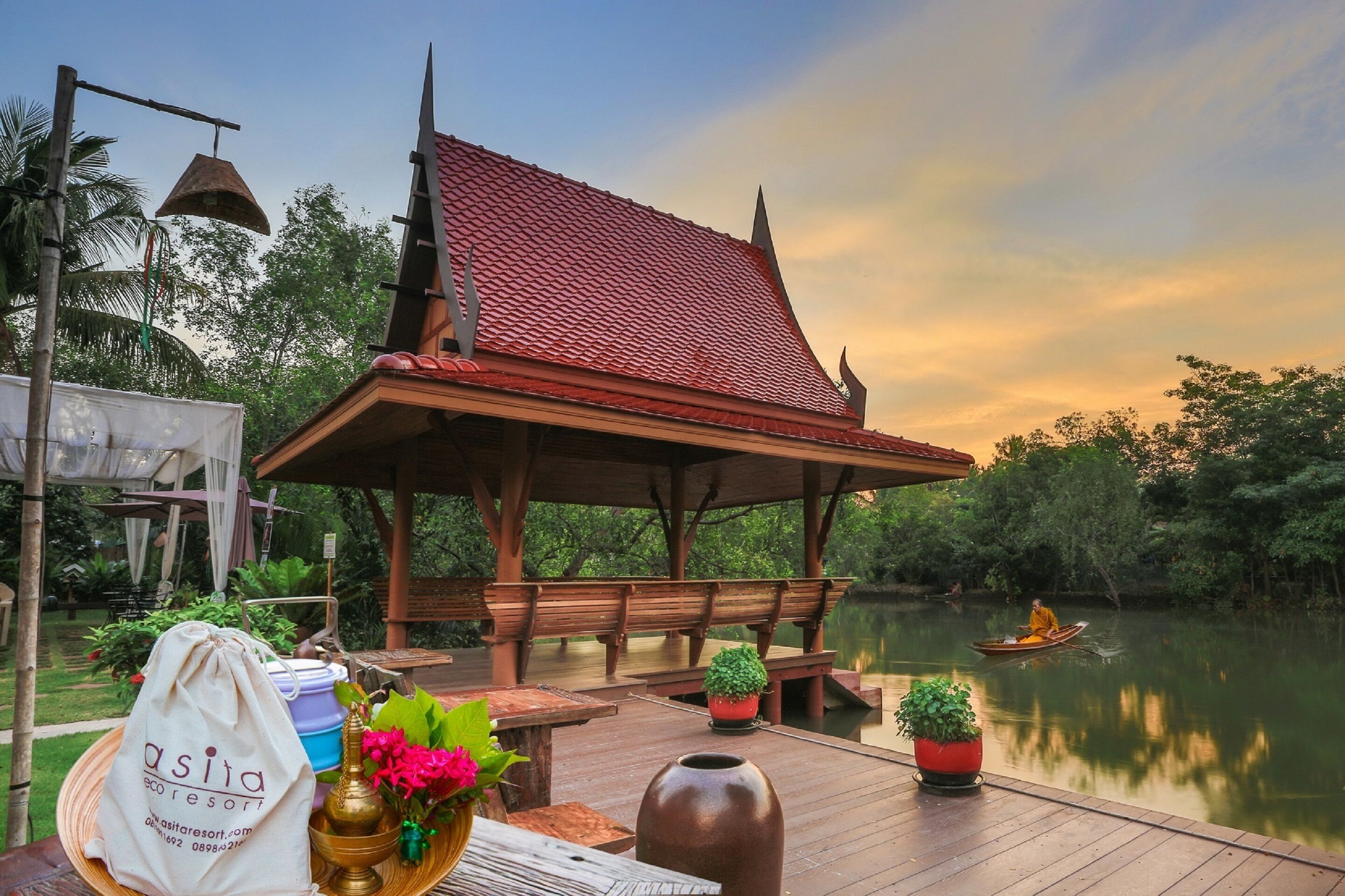A wooden pavilion with a tiled roof overlooking a calm river, surrounded by lush greenery.