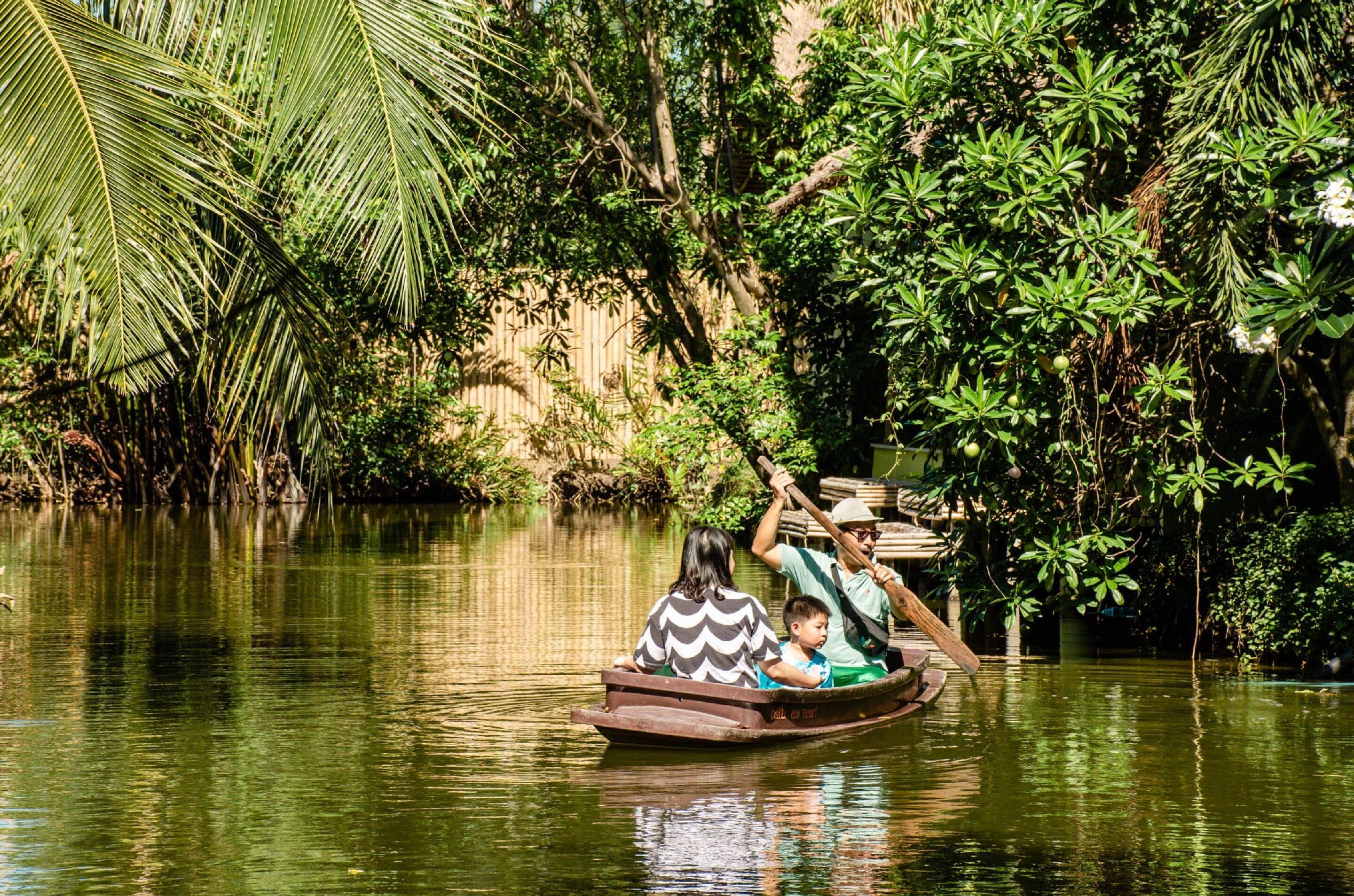 A boat with two passengers on a calm river surrounded by dense greenery.