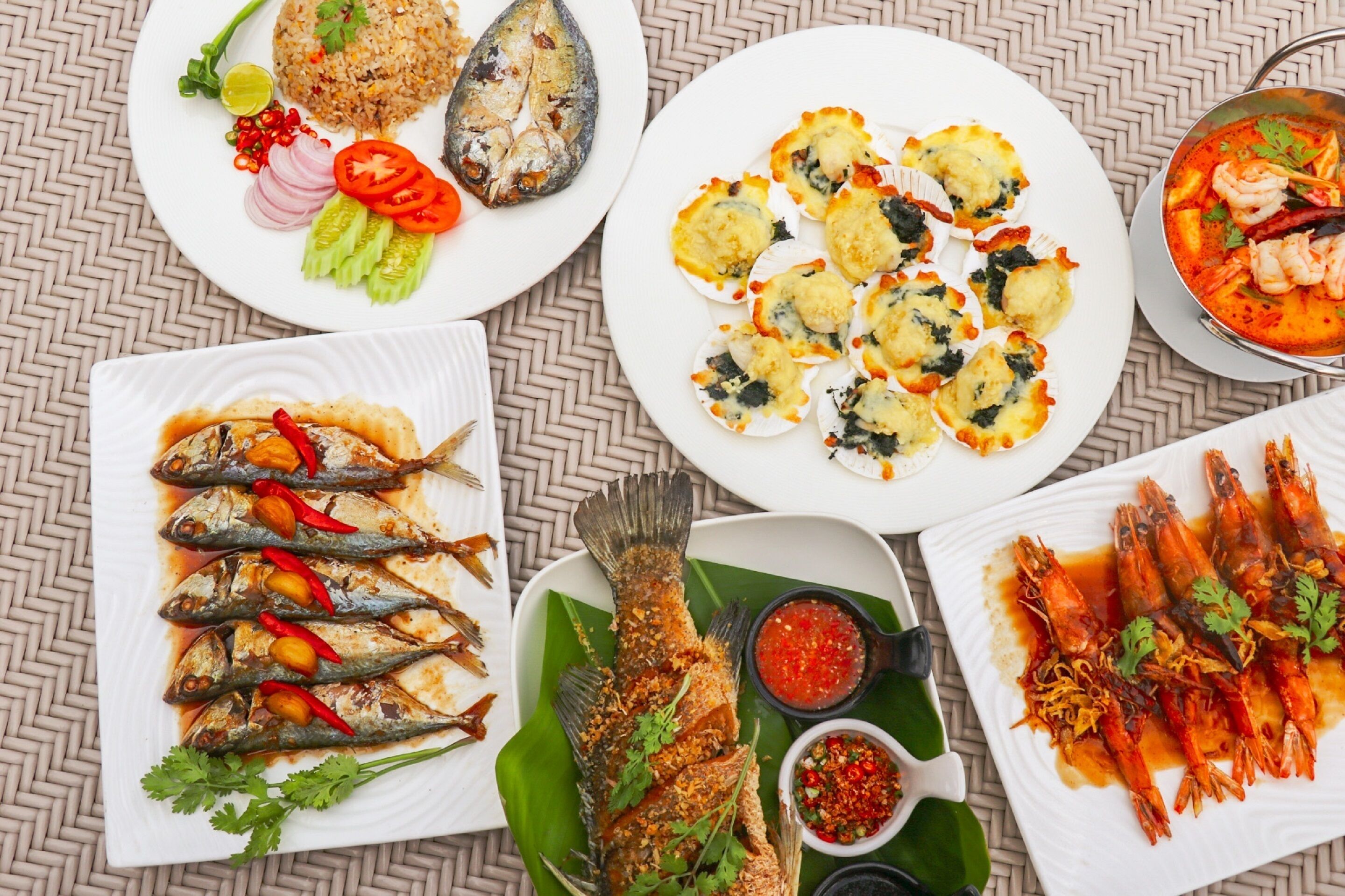 A variety of seafood dishes including fried fish, shrimp, and a fish curry, served on white plates with garnishes and condiments.