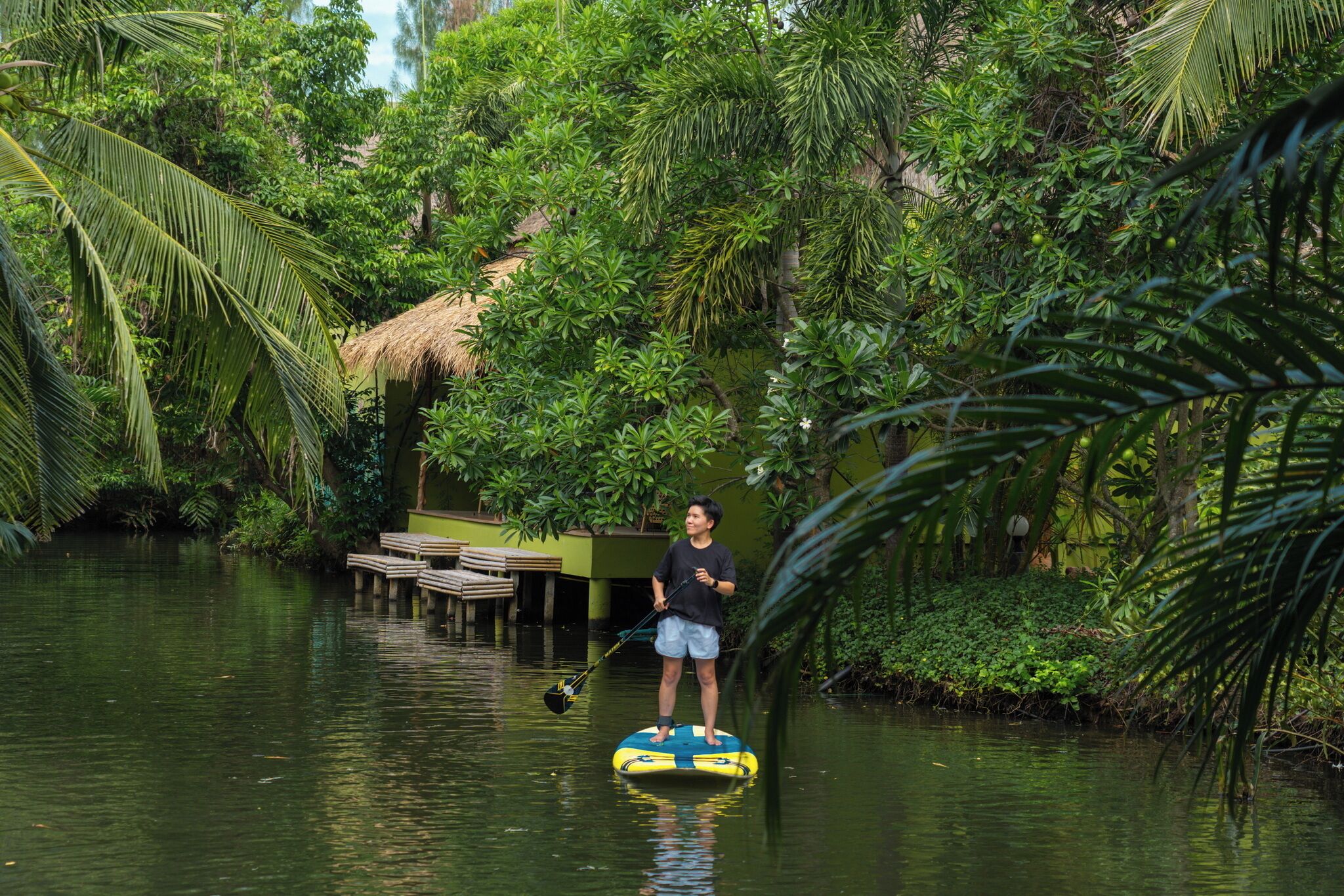 A person standing on a paddleboard in a water body surrounded by dense greenery.