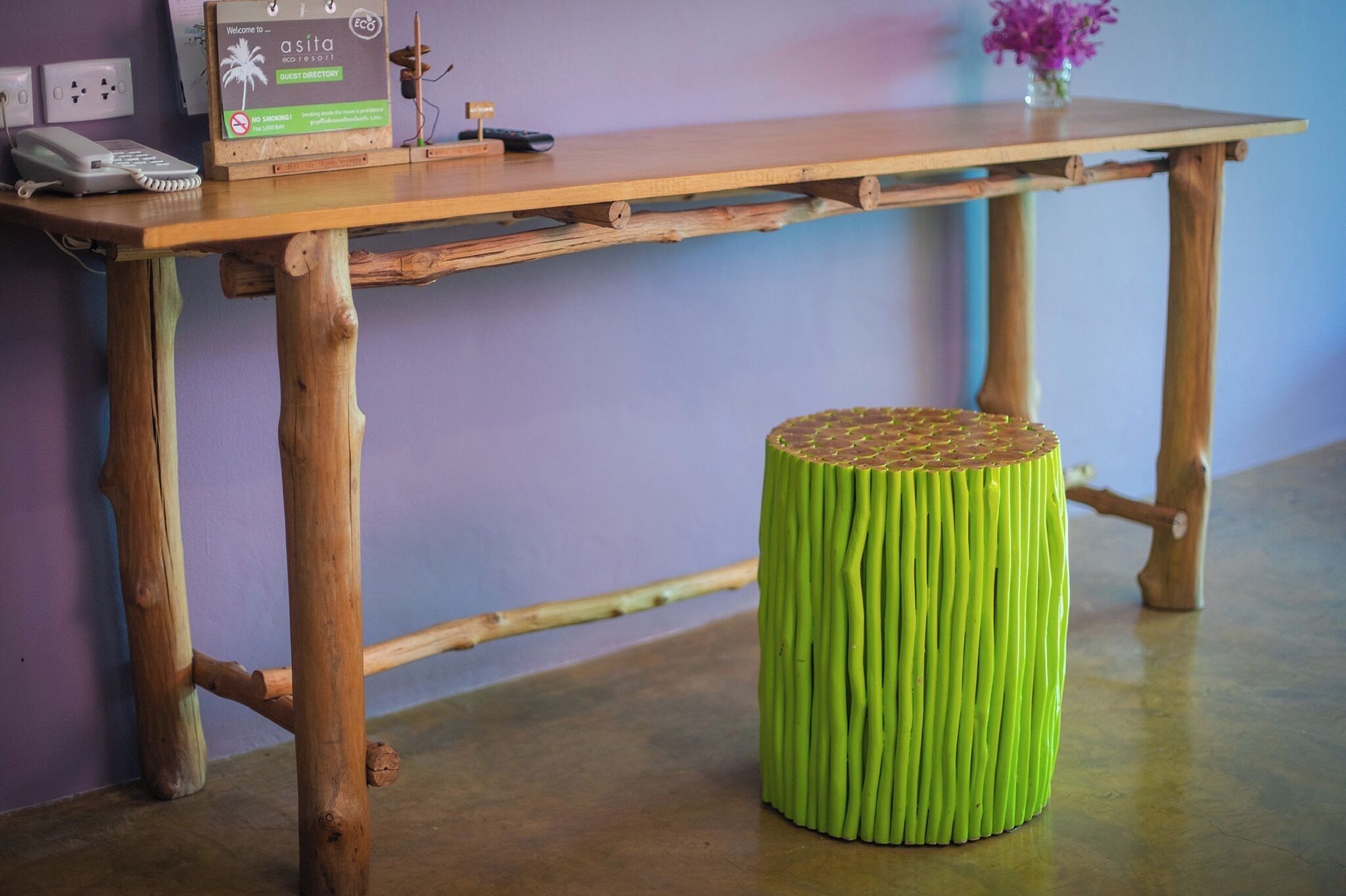 A wooden table with a sign, a phone, and a green stool.