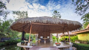 Un espacio al aire libre con techo, mesas y sillas, rodeado de follaje y una masa de agua.