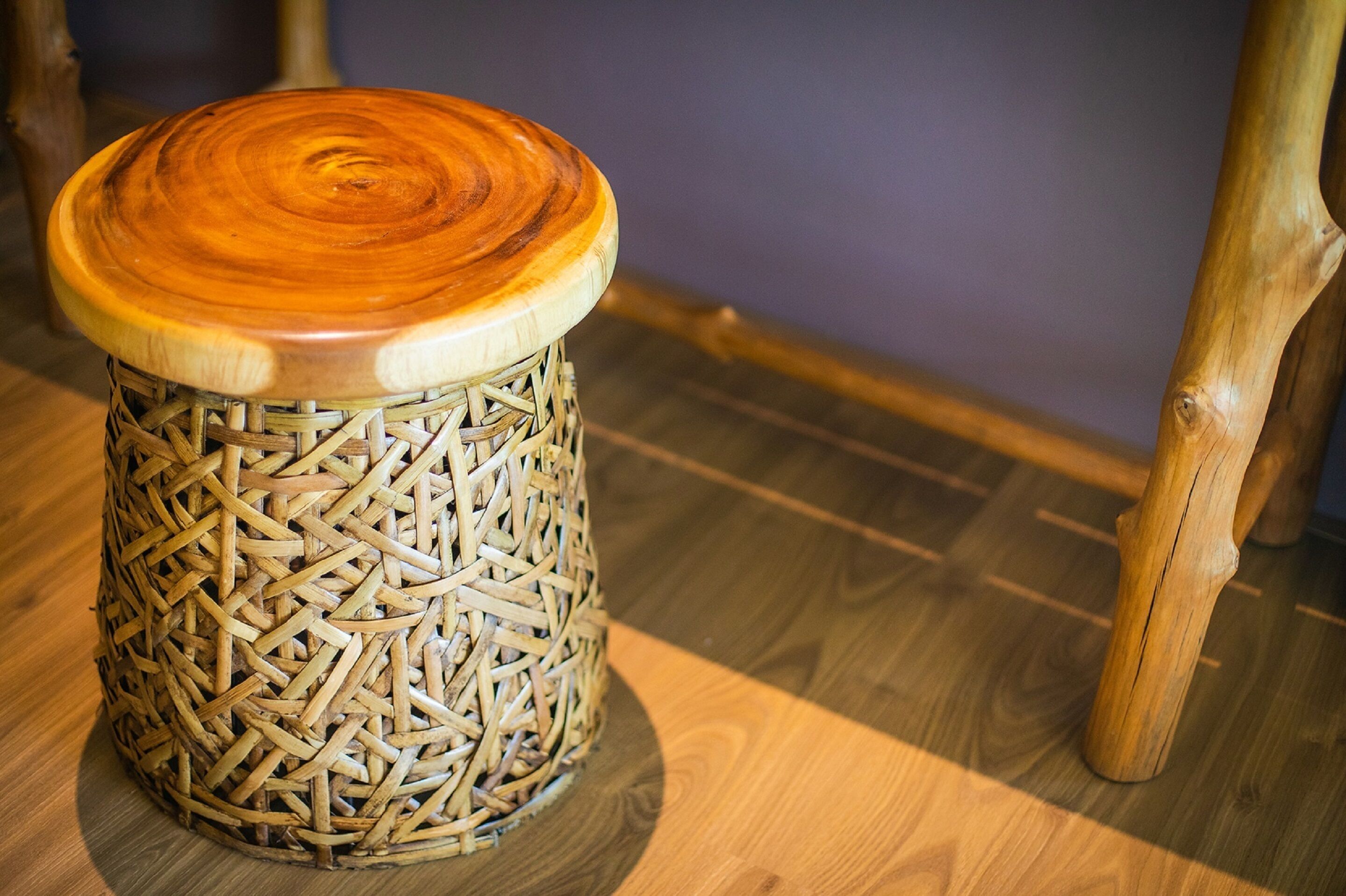 A woven stool with a wooden top, placed on a wooden floor.