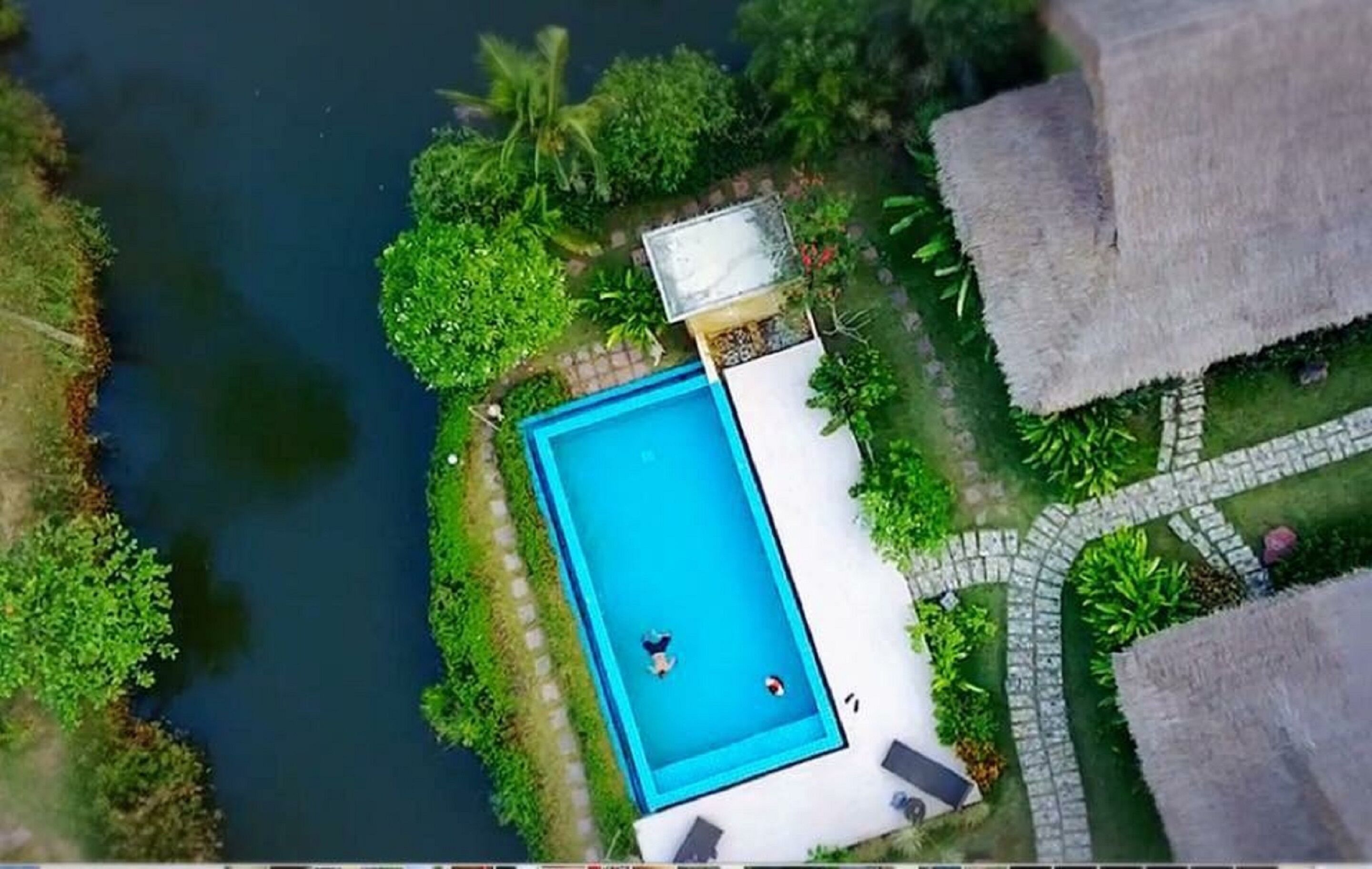 An aerial view of a swimming pool surrounded by lush greenery and a river.