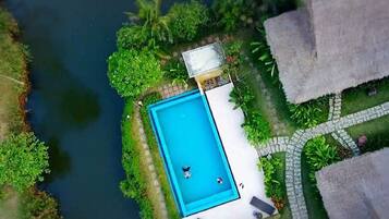 An aerial view of a swimming pool surrounded by lush greenery and a river.
