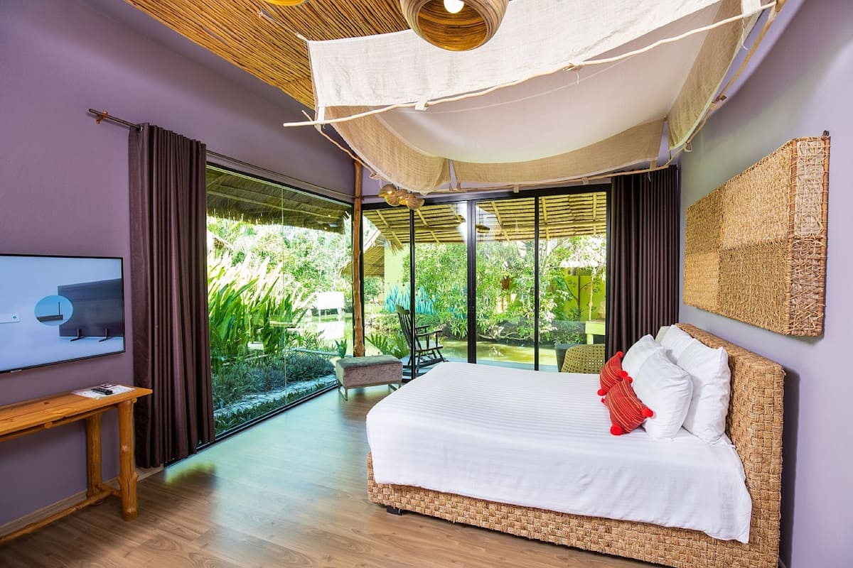 A bedroom with a large bed, a TV, and a view of greenery outside.