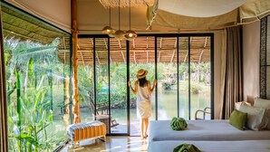 Una habitación con un gran ventanal corredizo que da a un espacio exterior privado con piscina y abundante vegetación.