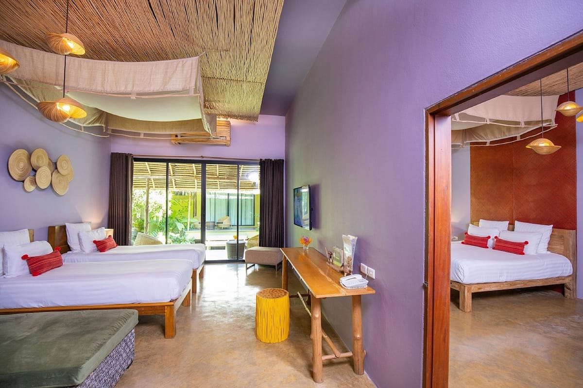 A hotel room with two beds, a wooden desk, a TV, and a large window with a view of greenery.
