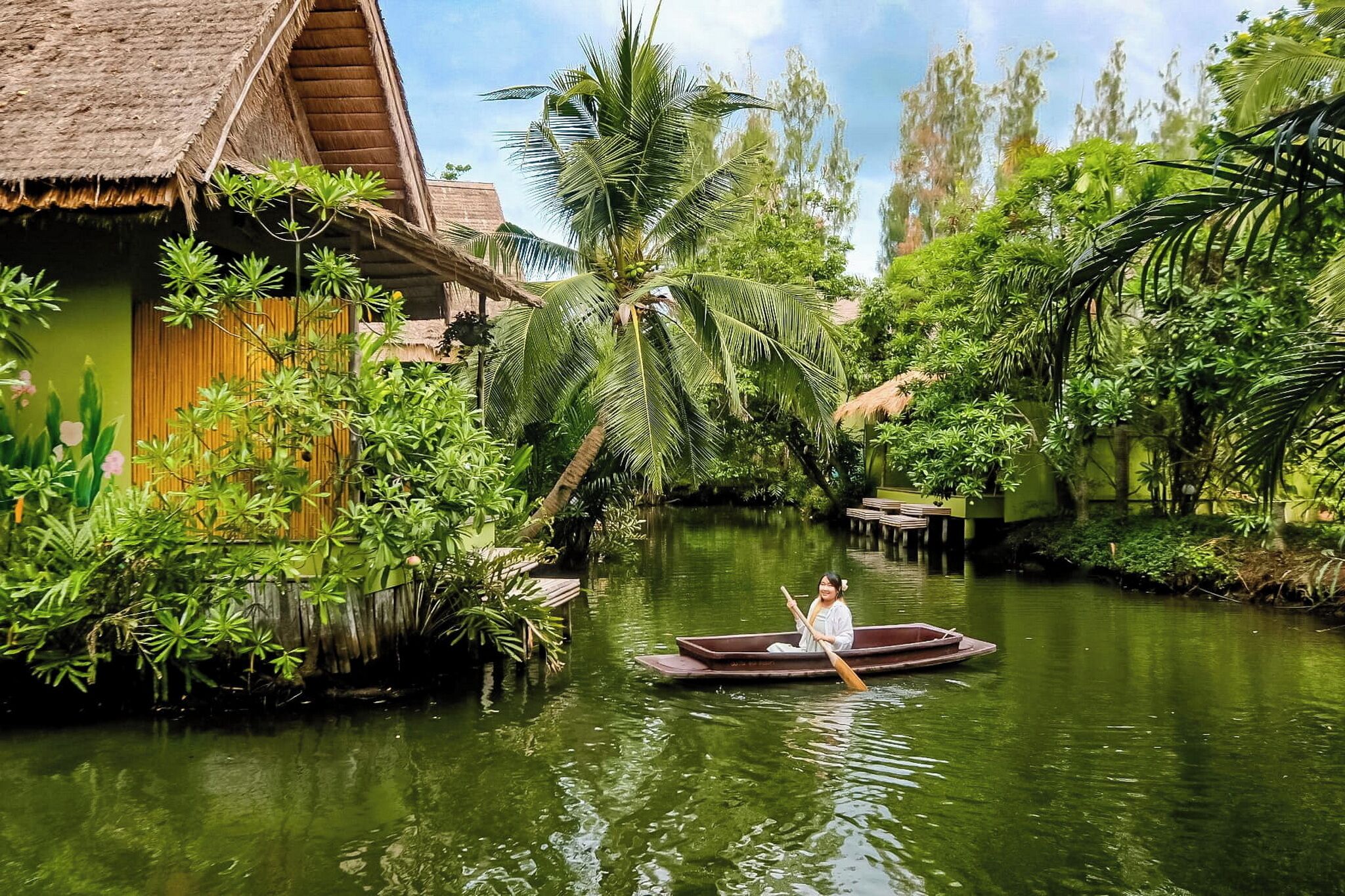 Ein Fluss mit einem Boot, umgeben von üppiger Vegetation und traditioneller Architektur.