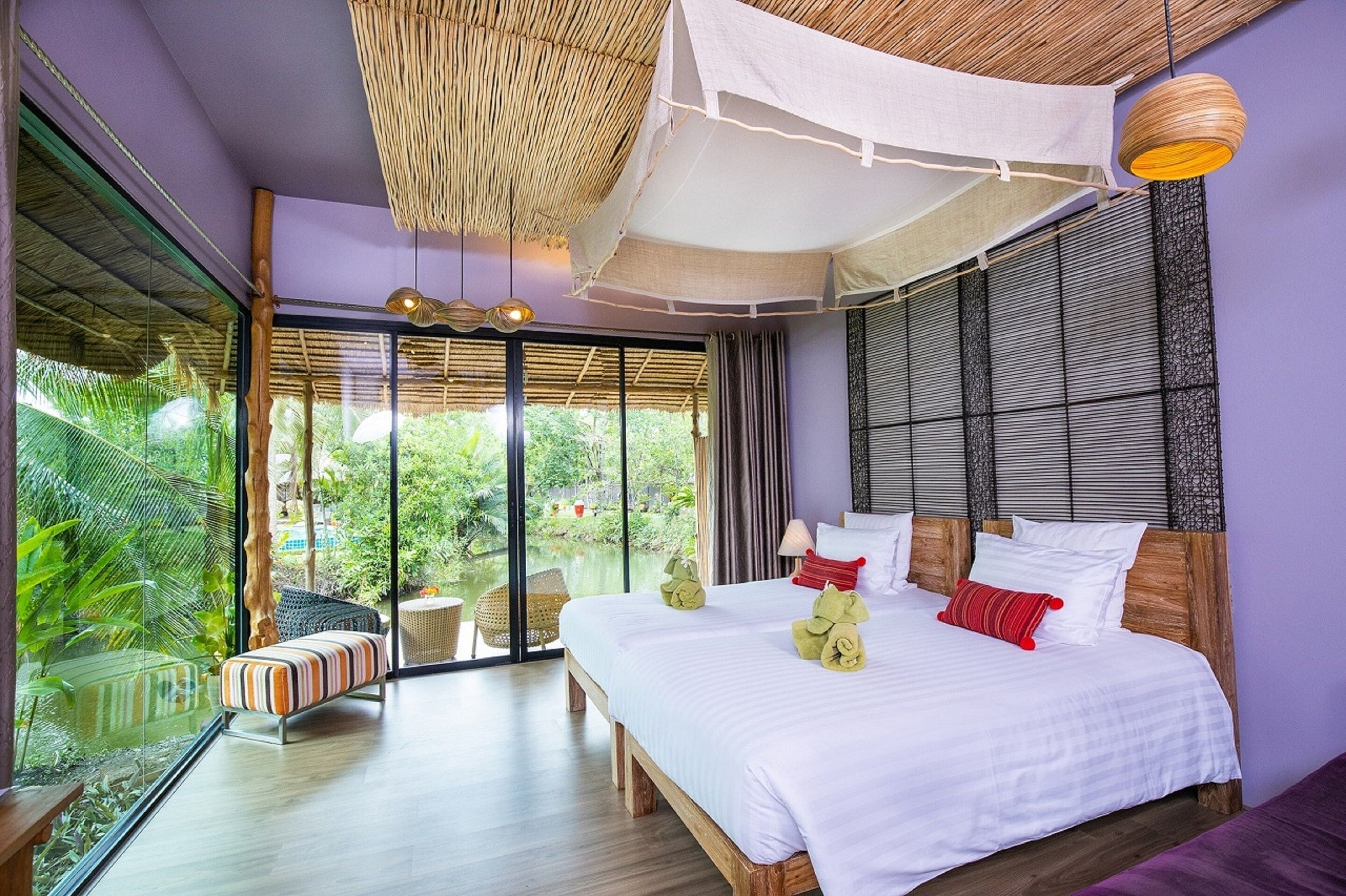 A modern bedroom with a large bed, a glass door leading to a garden, and a view of greenery outside.