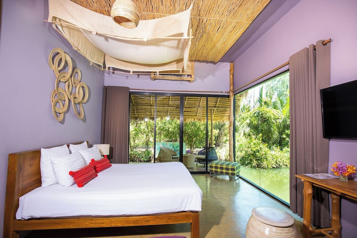 A bedroom with a large bed, a television, and a view of greenery through the window.