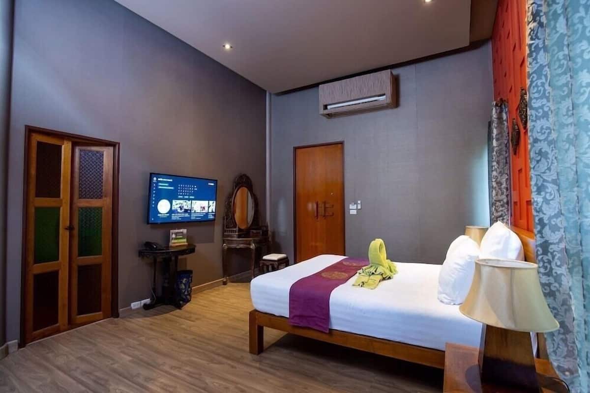 A hotel room with a bed, a television, an air conditioning unit, a wooden door, and a small table.