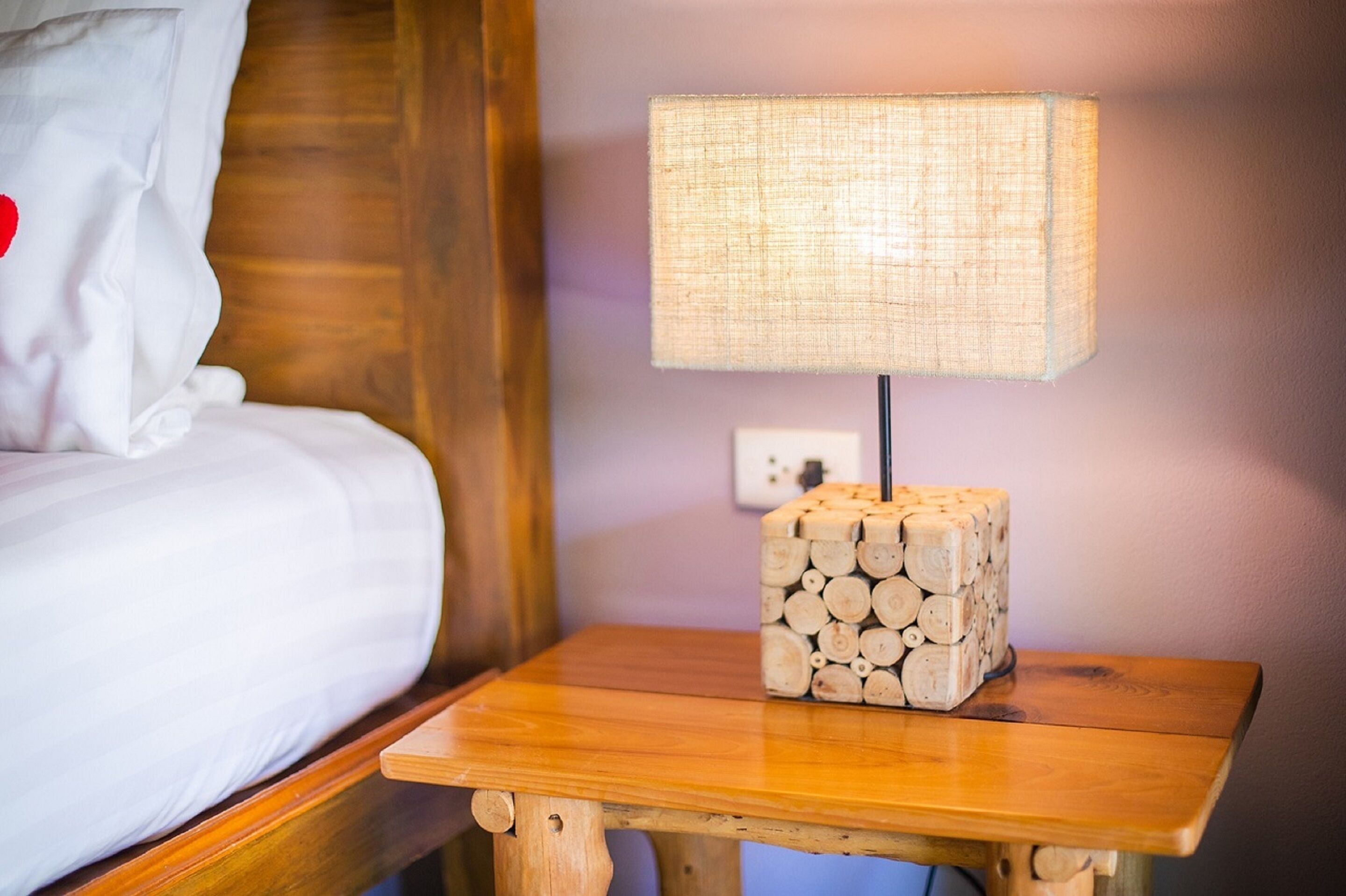 A wooden bedside table with a lamp and a stack of logs.