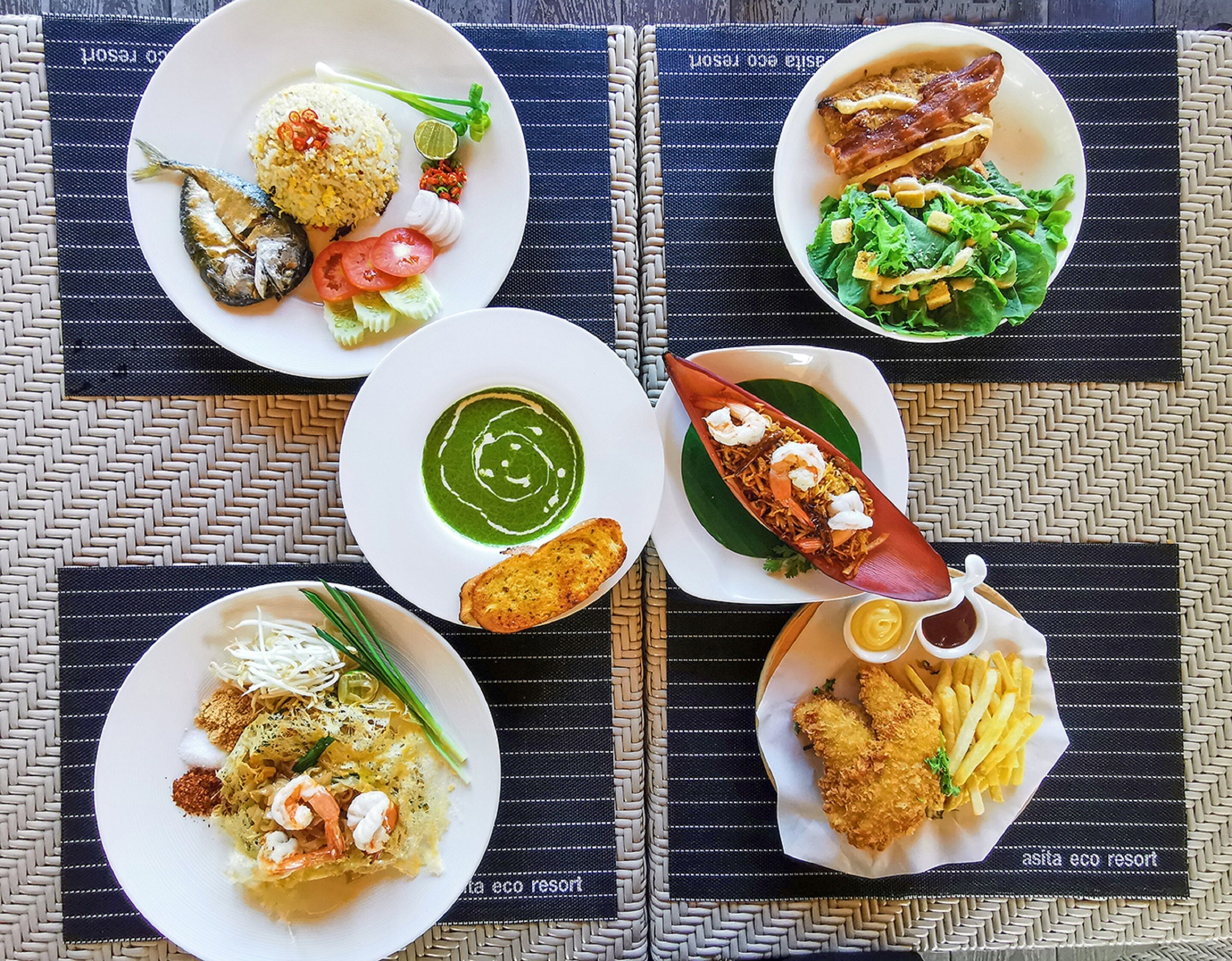 A table with various dishes including rice, fish, and fried items, set on a woven placemat.