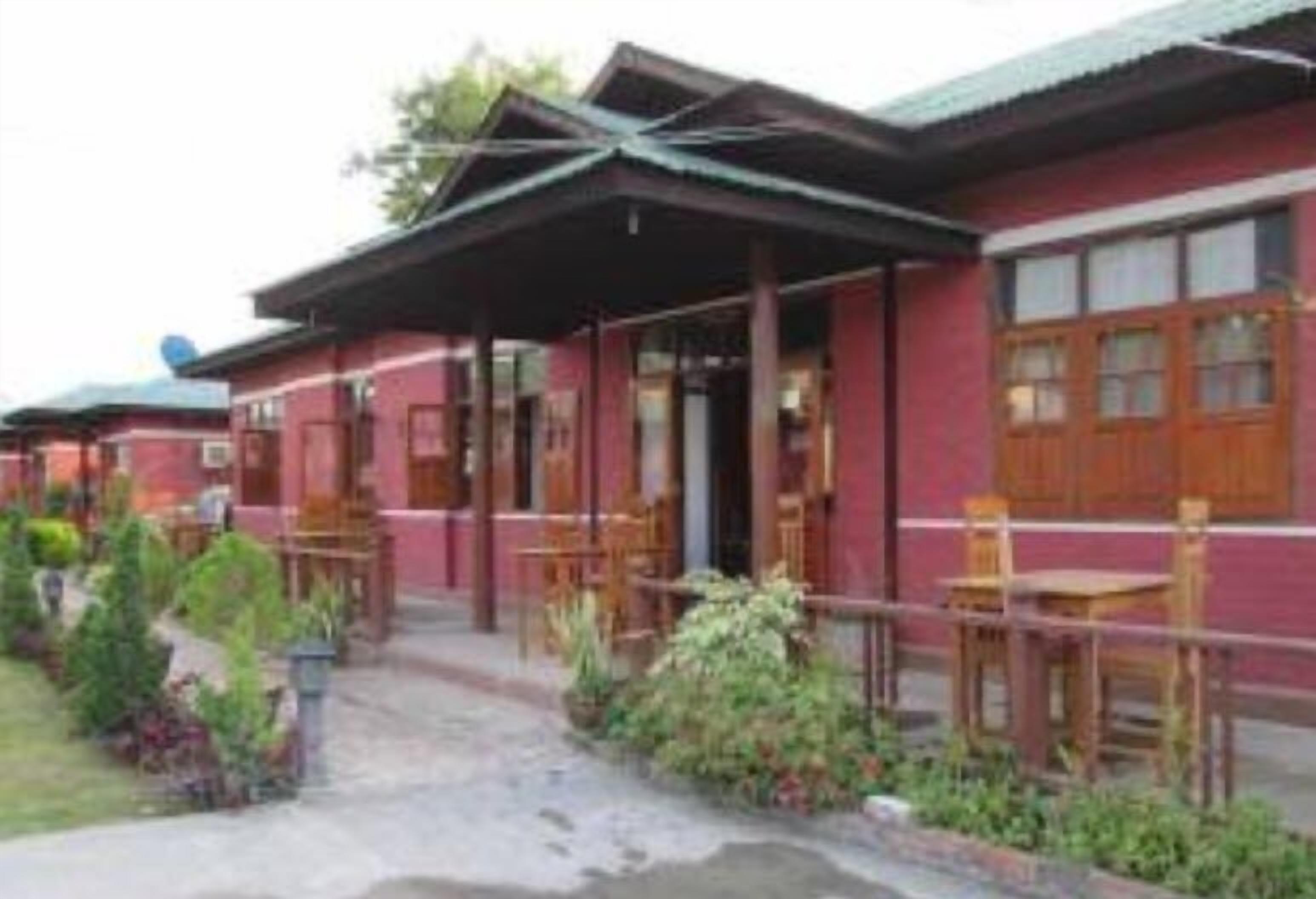 A building with a red exterior, wooden doors, and a covered outdoor seating area with tables and chairs.