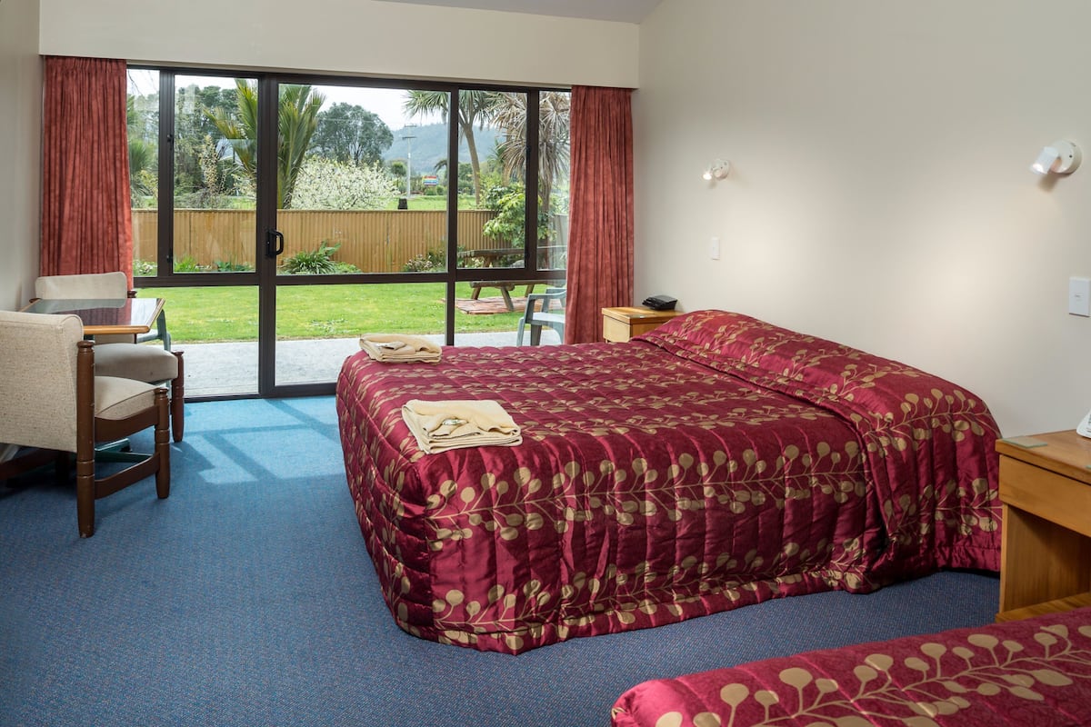 Une chambre d’hôtel avec un grand lit, un bureau et une chaise. Une porte-fenêtre coulissante donne accès à un balcon offrant une vue sur la verdure.