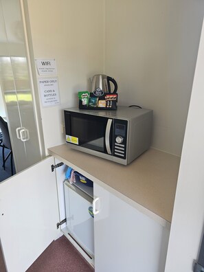 A kitchenette with a microwave, a coffee maker, and a paper recycling bin. - Karamea Hotel (Karamea)