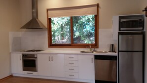 Een moderne keuken met witte kasten, een roestvrijstalen fornuis, een inbouwoven, een magnetron en een raam met uitzicht op bomen.