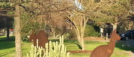 En skulptur föreställande en kaktus, en skulptur föreställande ett rådjur och ett träd i en parkmiljö.