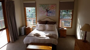 Een goed verlichte slaapkamer met een groot bed, twee nachtkastjes, een radiator en een raam met een glas-in-lood ontwerp van een boom.