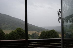 A view from a window overlooking a hilly landscape with trees and a distant building. - Eagles Nest (Merrijig)