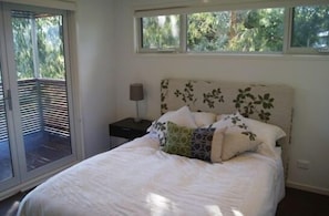 Un dormitorio con cama, mesita de noche, lámpara y ventana con persianas.