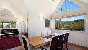 A spacious dining area with a wooden table and chairs, large windows offering a view of a mountainous landscape, and a red rug on the floor. - Jarrah Lodge (Merrijig)
