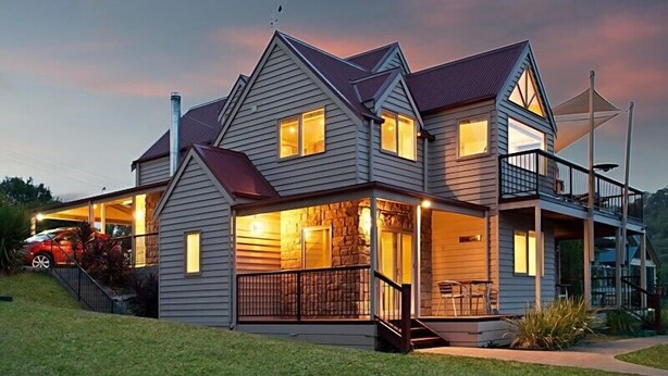 A two-story house with a covered porch, a stone fireplace, and a car parked in the driveway. - Jarrah Lodge (Merrijig)