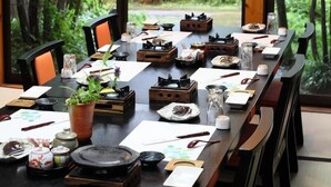 A dining table set in a room with a view of a forest.