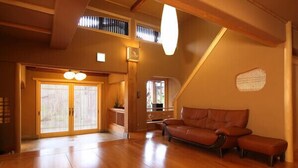 A spacious living area with a wooden floor, a brown leather sofa, and a large window.