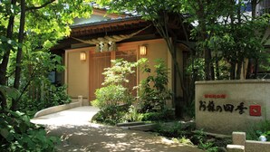 A traditional Japanese building with a wooden entrance, surrounded by lush greenery and a stone pathway.