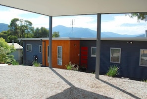 A modern house with a covered patio, a wooden door, and a view of mountains.