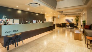 Zona de recepción con mostrador identificado como "WINNERS", dos taburetes, una mesa de recepción, área de asientos con sillas y un sofá, y una planta decorativa.