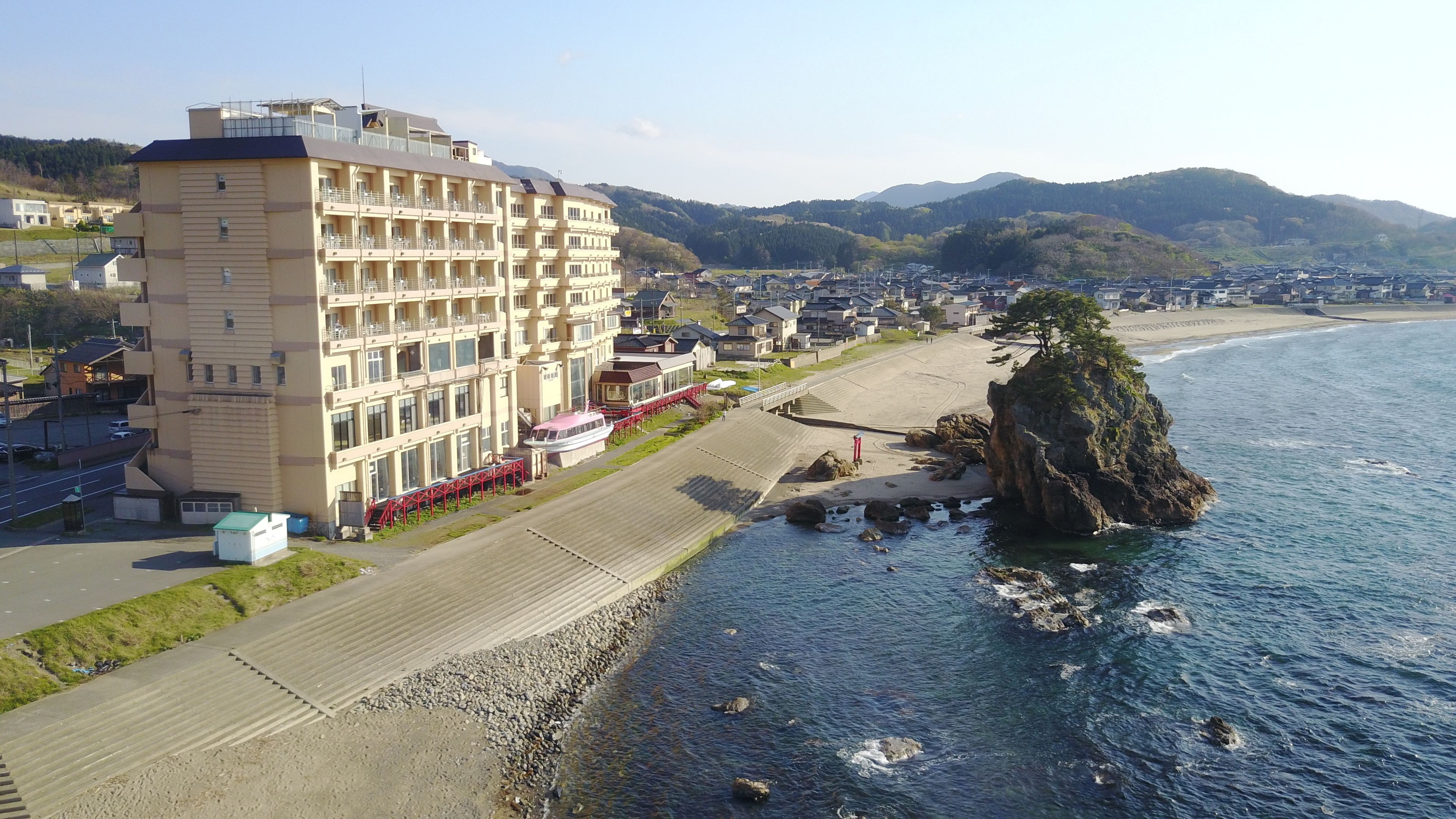 Un hotel frente al mar con varios pisos, un paseo marítimo y un promontorio rocoso.