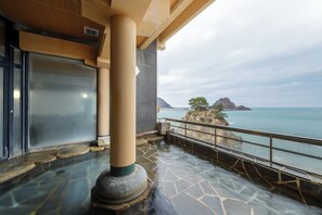 Un área de spa con suelo de piedra, un pilar grande y vistas al mar y afloramientos rocosos.