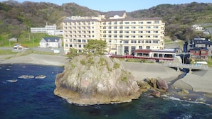 A coastal hotel with multiple floors, a rocky island in the foreground, and a bridge connecting to the mainland. - Hotel Yaotome (Tsuruoka)