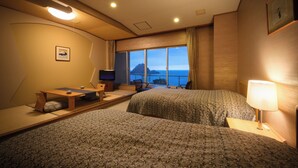A hotel room with two beds, a desk, a chair, a TV, and a large window with a view of the sea. - Hotel Yaotome (Tsuruoka)
